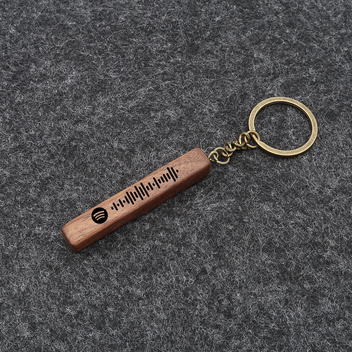 Spotify-avainrengas, johon on kaiverrettu Spotify-koodi ja nimi. Aidosta puusta valmistettu puupalkki